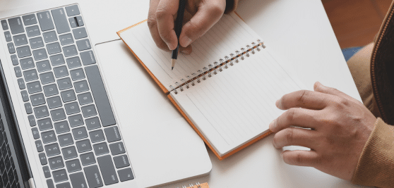Writing in notebook by laptop